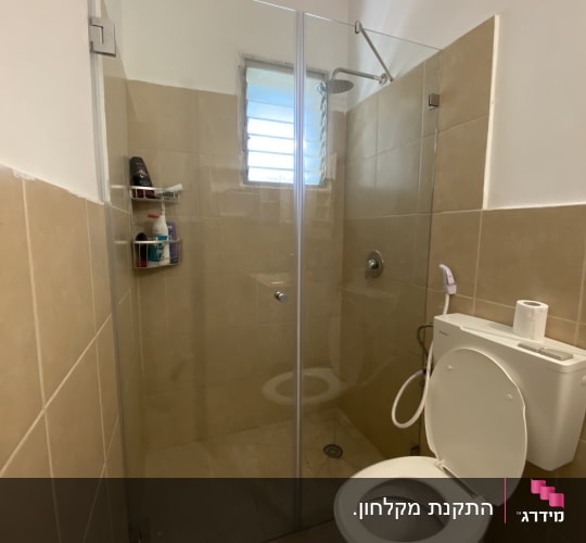 מקלחון חזית מזכוכית שקופה מותקן בחדר רחצה עם אריחים בהירים